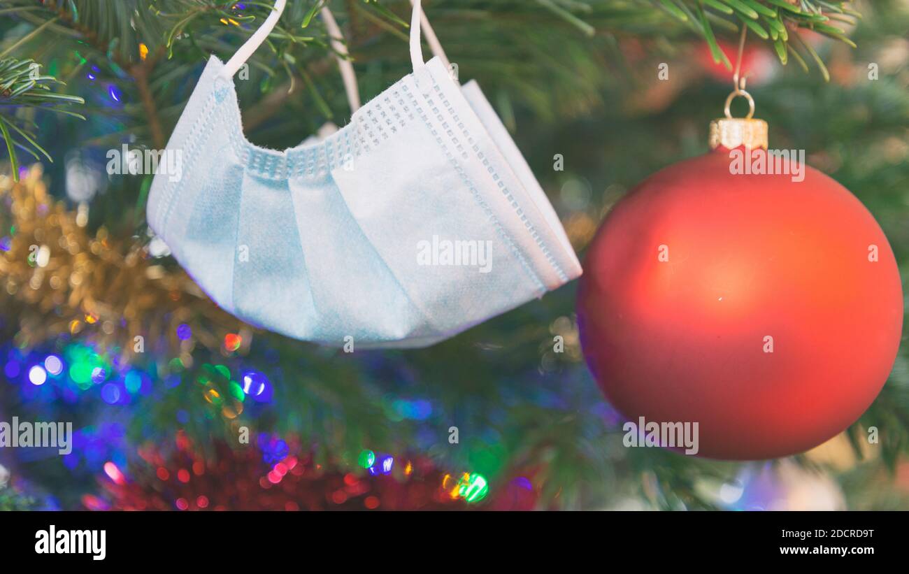 Maschera protettiva appesa all'albero di Natale. Festeggiando le vacanze durante la pandemia del coronavirus. Foto Stock