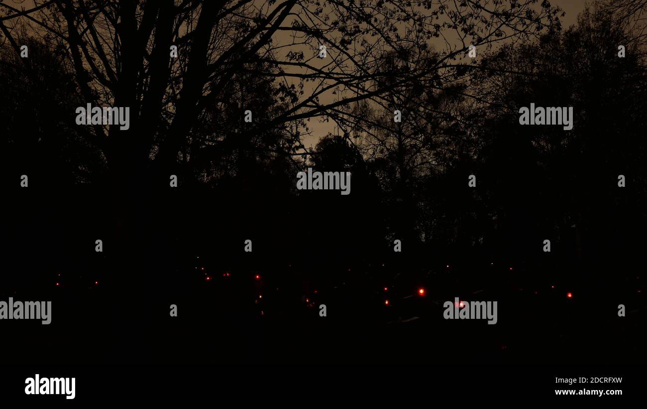 Cimitero con candele rosse sulle tombe di notte con un cielo inquietante sullo sfondo Foto Stock