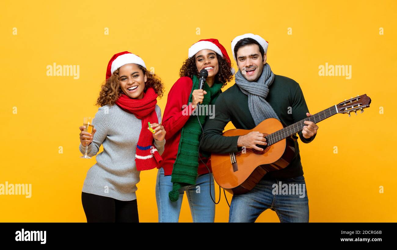 Ritratto di diversi amici che hanno partito cantando bevendo e festeggiando Natale su sfondo isolato giallo Foto Stock