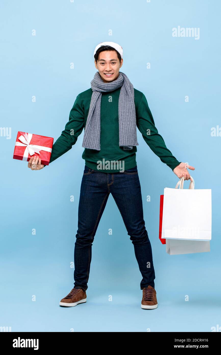 Sorpreso felice uomo asiatico tenendo scatola regalo di Natale e shopping borse in blu chiaro studio isolato sfondo Foto Stock