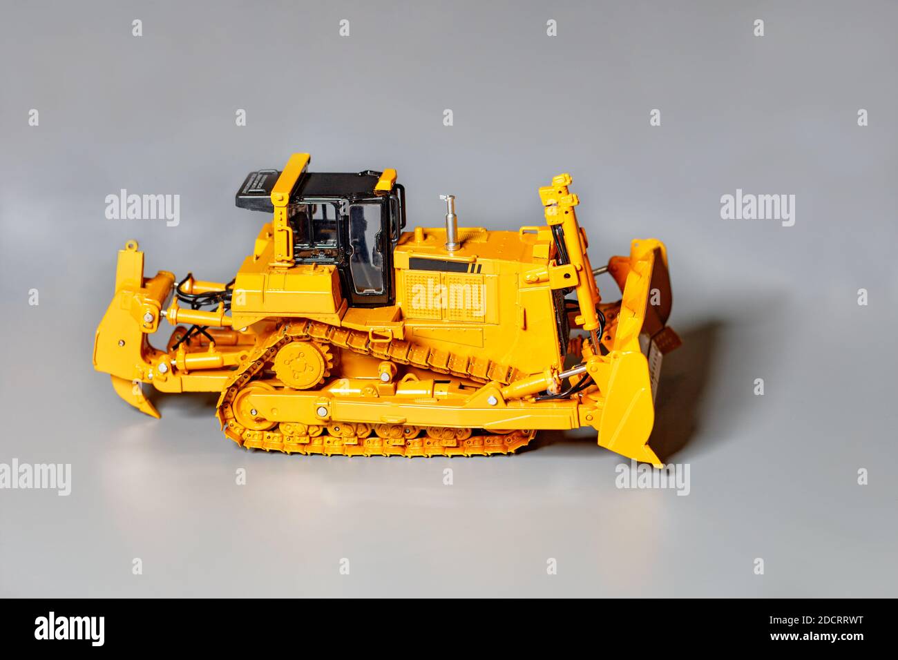 Modello giocattolo di un bulldozer giallo su sfondo grigio chiaro, fuoco selettivo, spazio di copia. Foto Stock
