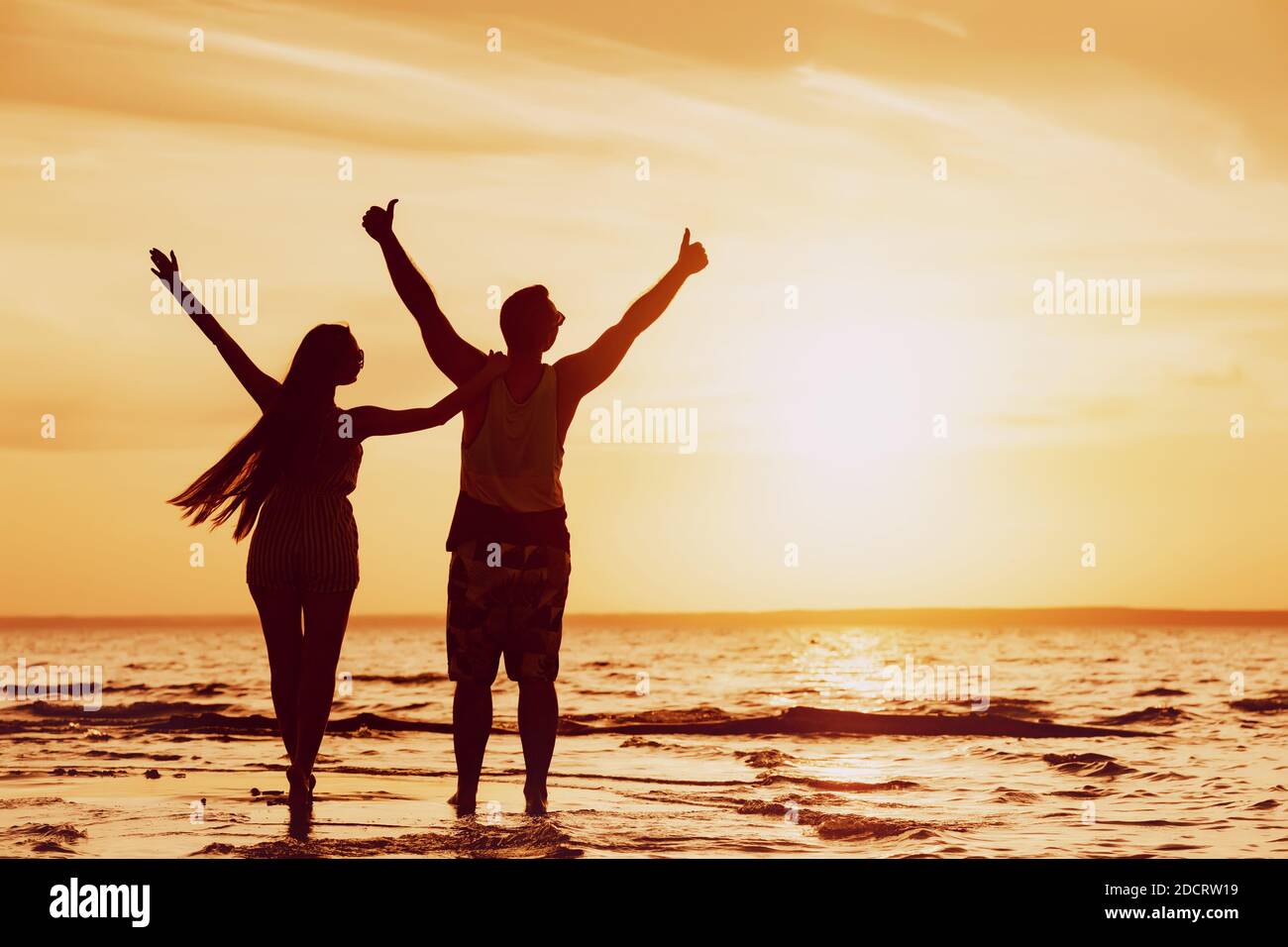 Happy Couple si erge con le braccia sollevate alla spiaggia del tramonto Foto Stock