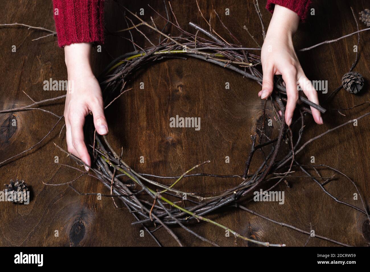 Donna che fa la corona di natale dai rami della natura. Tavolo scuro in legno Foto Stock