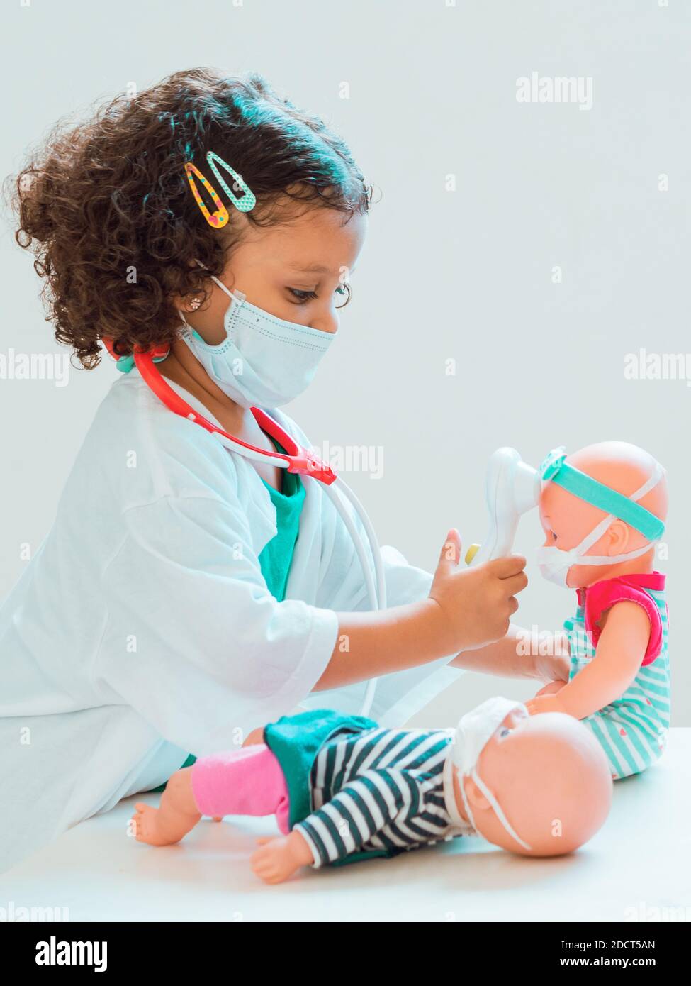Una bambina che gioca il medico controllare la febbre al suo paziente, tutti indossare maschere di protezione Foto Stock