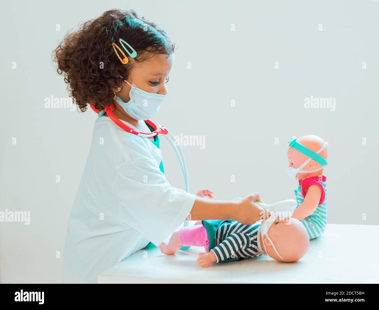 Una bambina che gioca il medico controllare la febbre al suo paziente, tutti indossare maschere di protezione Foto Stock