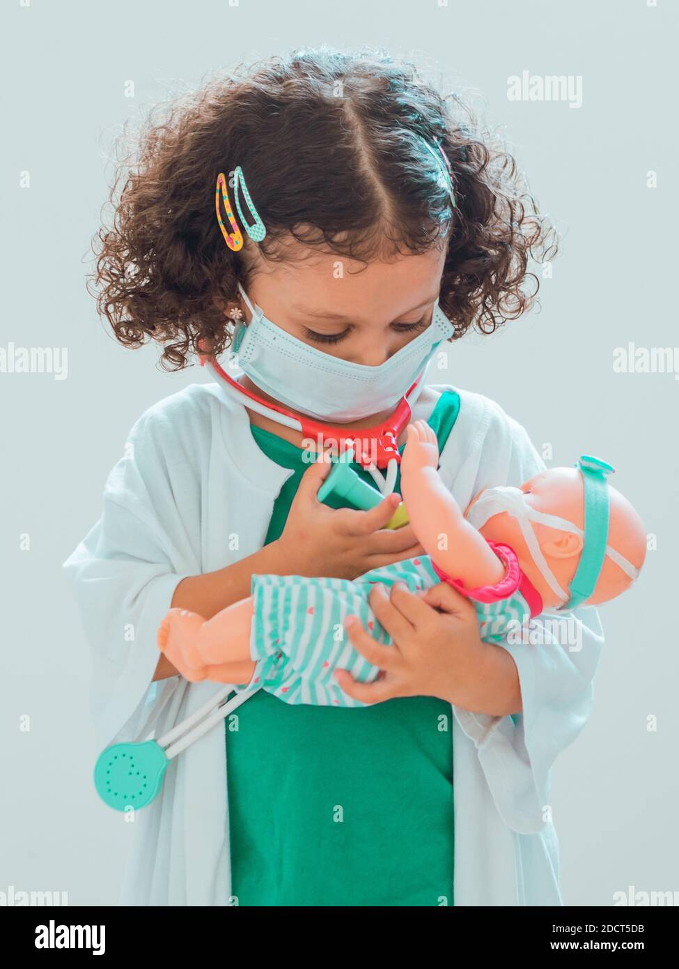 Una bambina che gioca il medico le dà un'iniezione al paziente, tutti indossano maschere protettive Foto Stock
