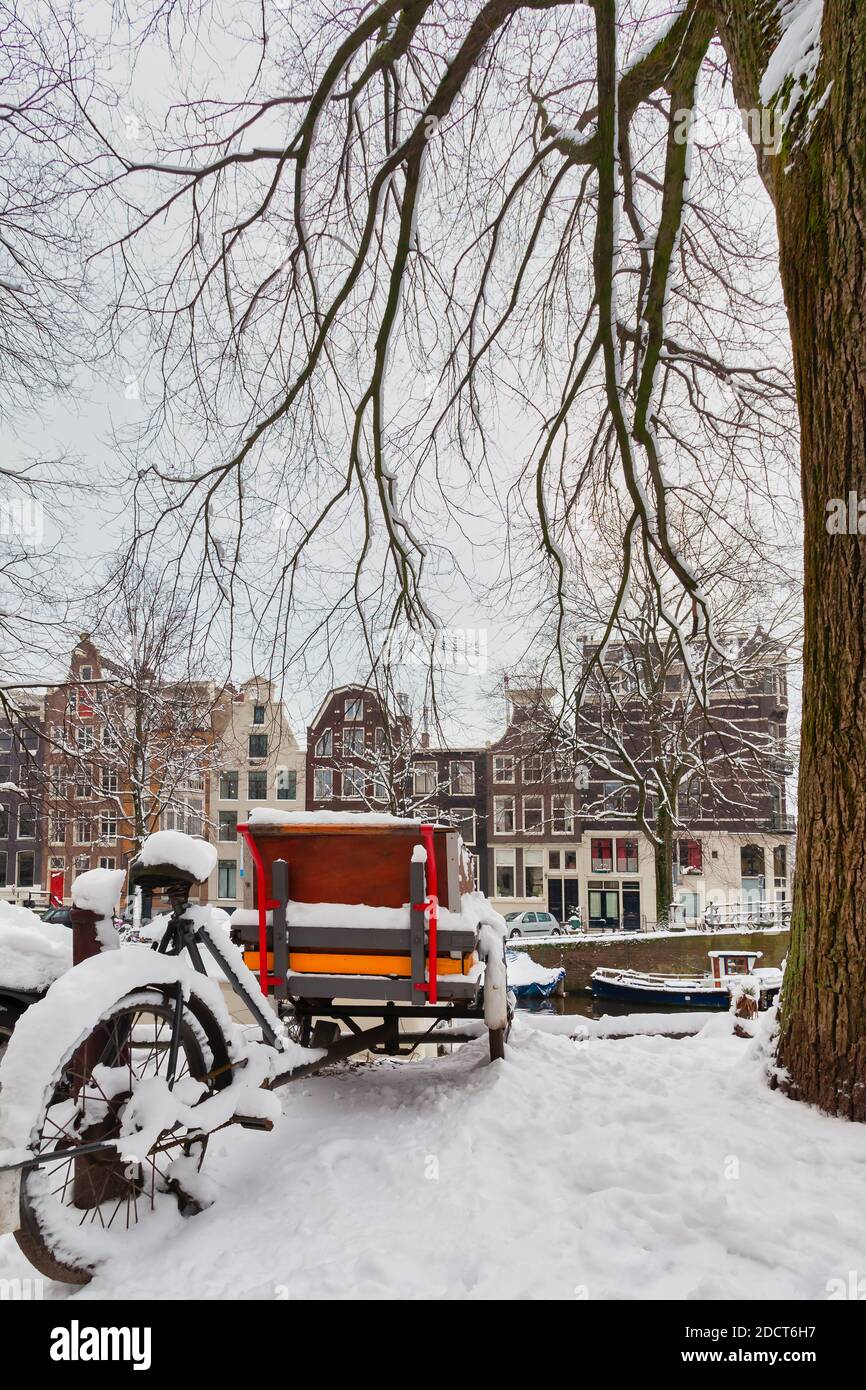 Bicicletta da carico parcheggiata coperta di neve davanti a un Canale di Amsterdam durante l'inverno Foto Stock