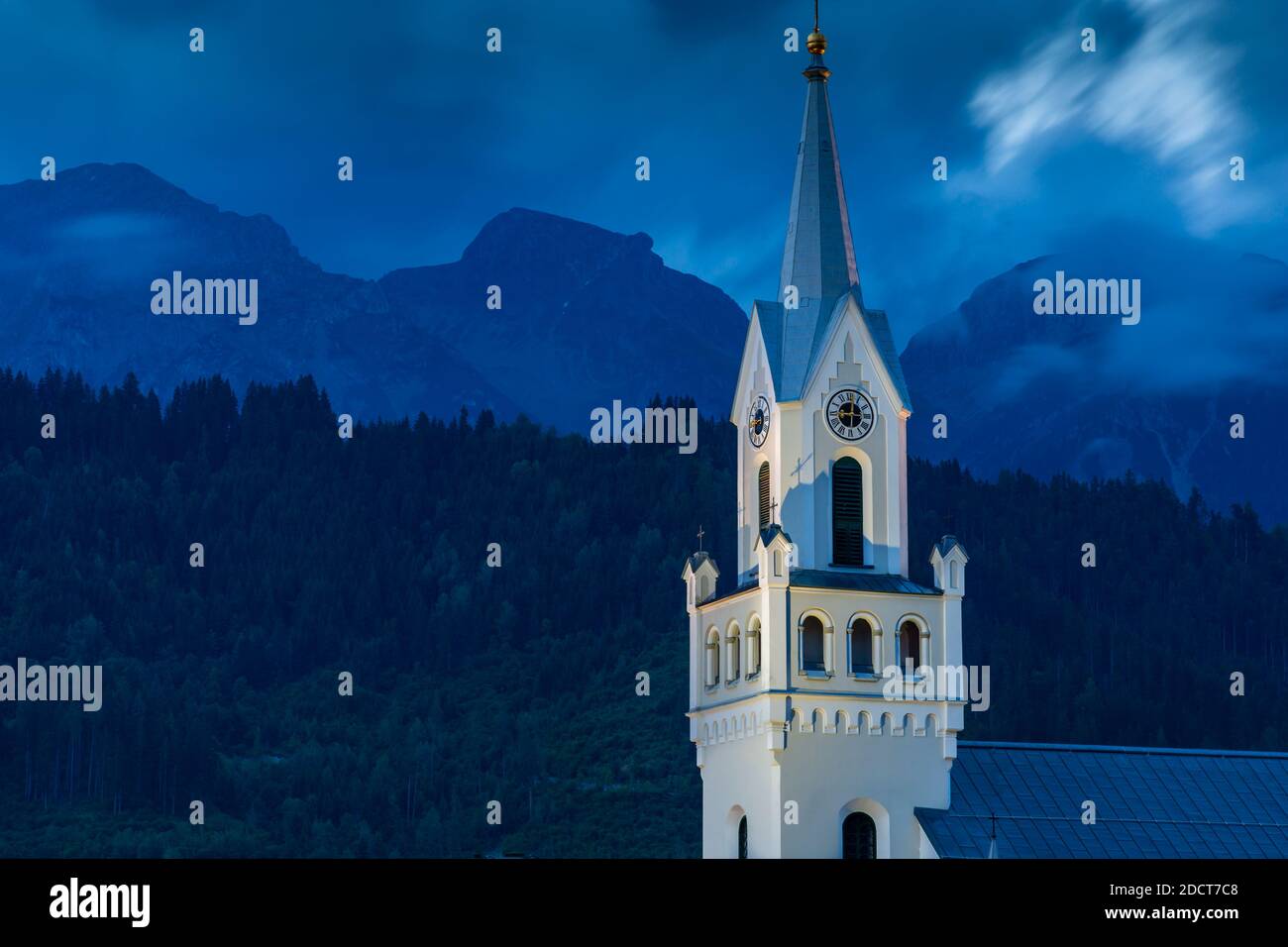 Vista della torre dell'orologio della chiesa con sfondo montuoso al tramonto, Schladming, Stiria, Tirolo austriaco, Austria, Europa Foto Stock