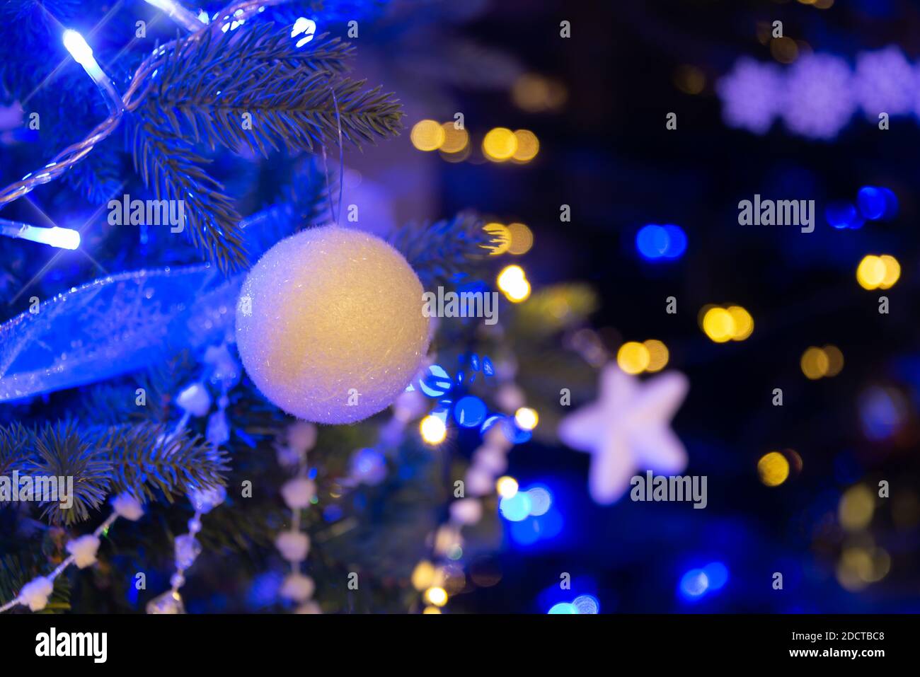 Pallina bianca appesa su un albero di Natale, ornamenti di Natale di notte, luci di vacanza blu e oro Foto Stock