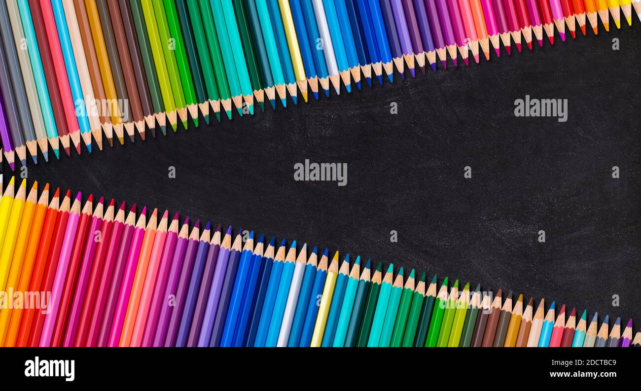 Bordo di colorate matite di legno in fila su una lavagna vuota, concetto di ritorno a scuola. Foto Stock