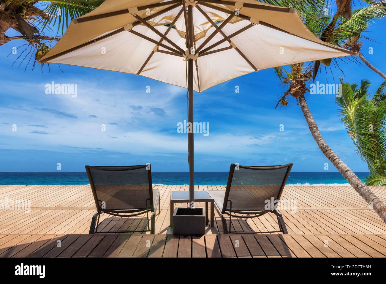 Spiaggia soleggiata con ombrellone e sedie a sdraio su pavimento in legno, palme e il mare turchese sull'isola Paradise. Foto Stock