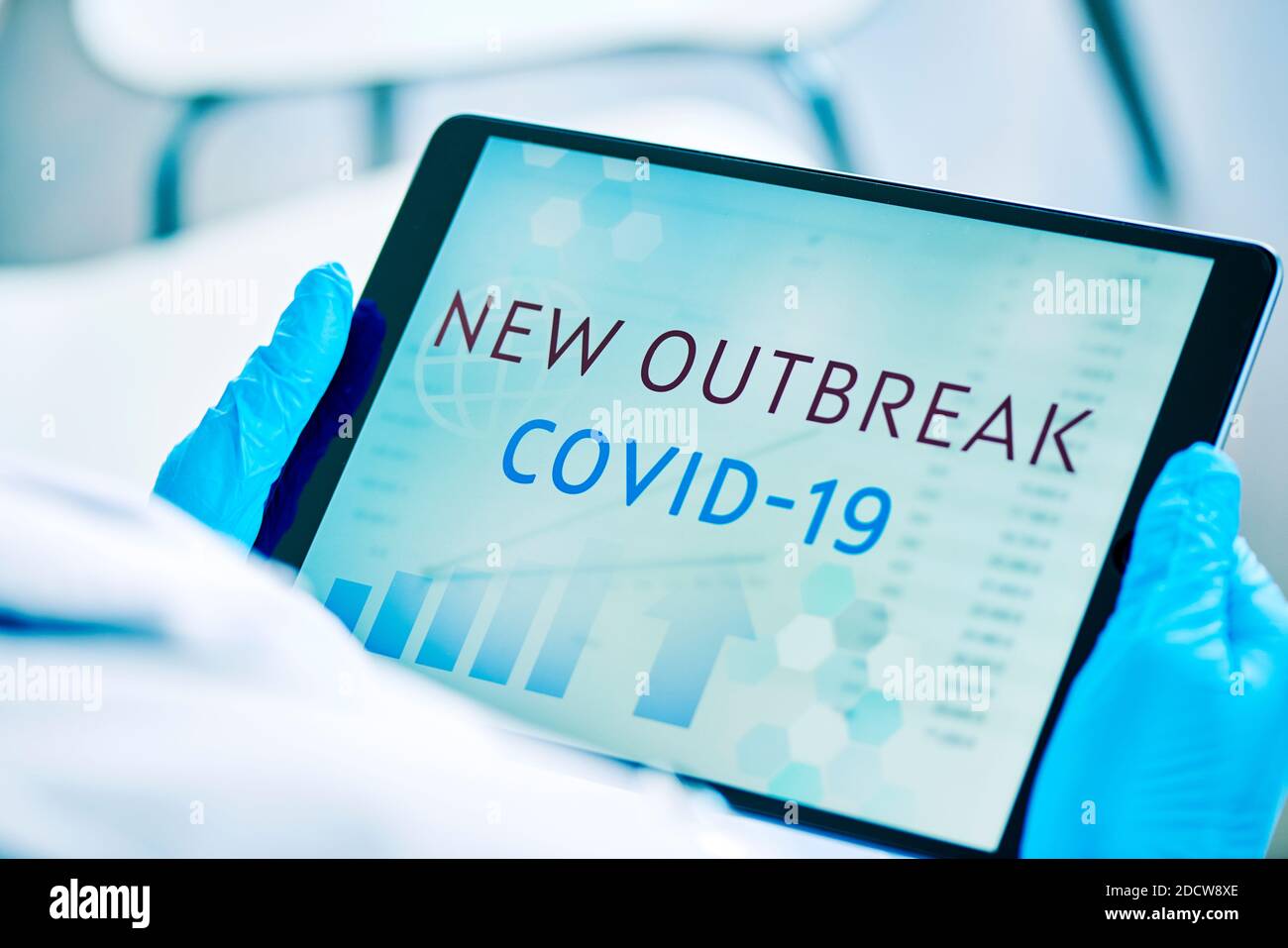primo piano di un medico, indossando guanti chirurgici blu, avendo una tavoletta digitale in mano con il testo covid-19 nuovo focolaio nel suo schermo Foto Stock