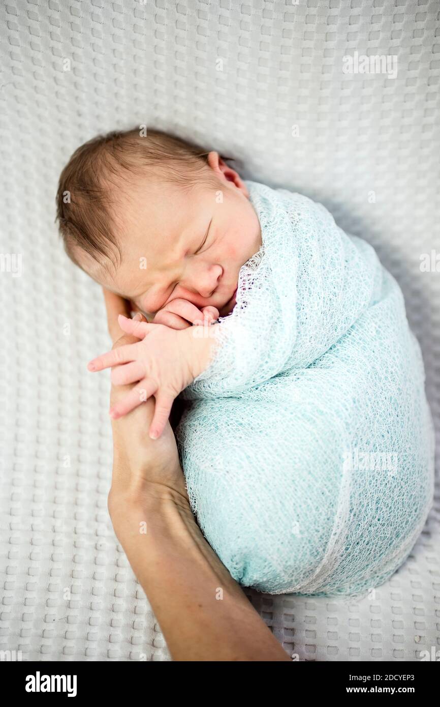 Cute bambino neonato addormentato avvolto in blu posa su la mano della madre Foto Stock