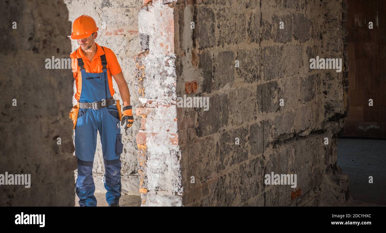 Caucasian Builder Contractor nel suo 40s e Old Building rimodellamento e restauro lavoro. Tema industriale. Ricostruendo mattoni di cemento invecchiato Casa costruita Foto Stock