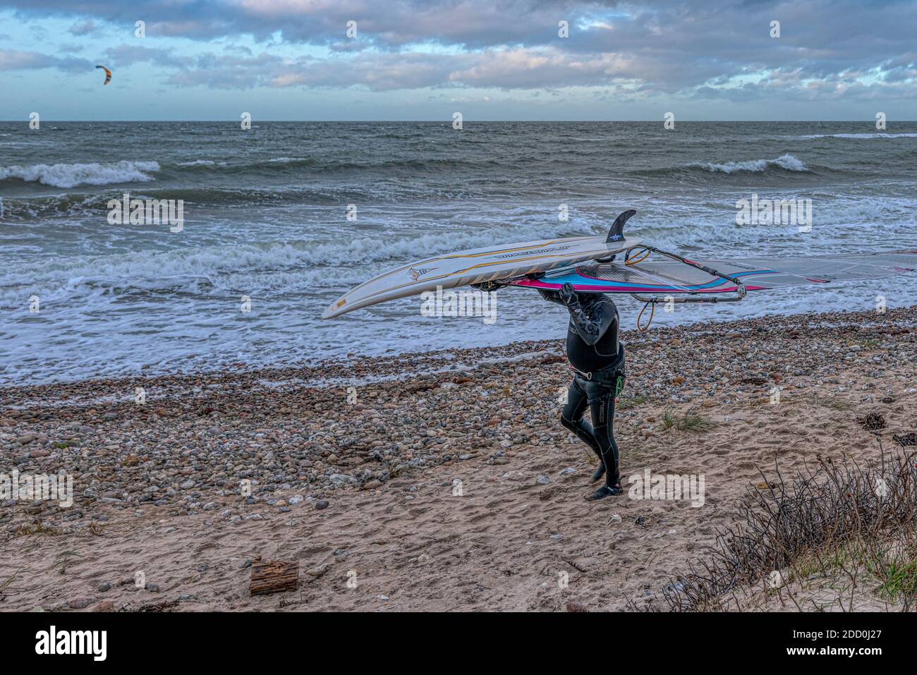 Il surfista anziano in costume da bagno nero cammina sulla riva e trasporta le sue attrezzature sulla testa, Smidstrup, Danimarca, 22 novembre 2020 Foto Stock