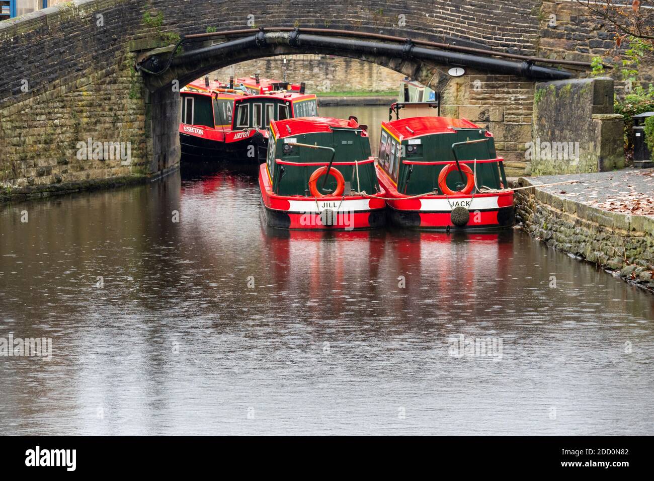 Barche strette dipinte di rosso e bianco sotto un ponte di canale sul canale di Leeds e Liverpool a Skipton , North Yorkshire UK Foto Stock