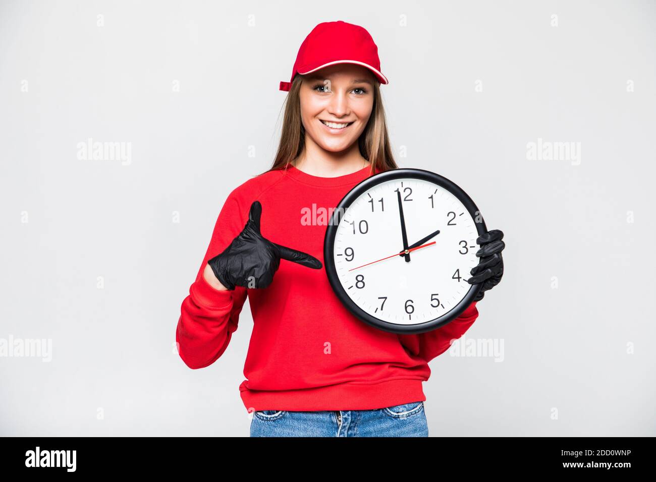 Donna di consegna in uniforme rossa isolata su sfondo bianco. Donna professionale in berretto, t-shirt, jeans che lavorano come corriere o commerciante, tenendo clo rotondo Foto Stock