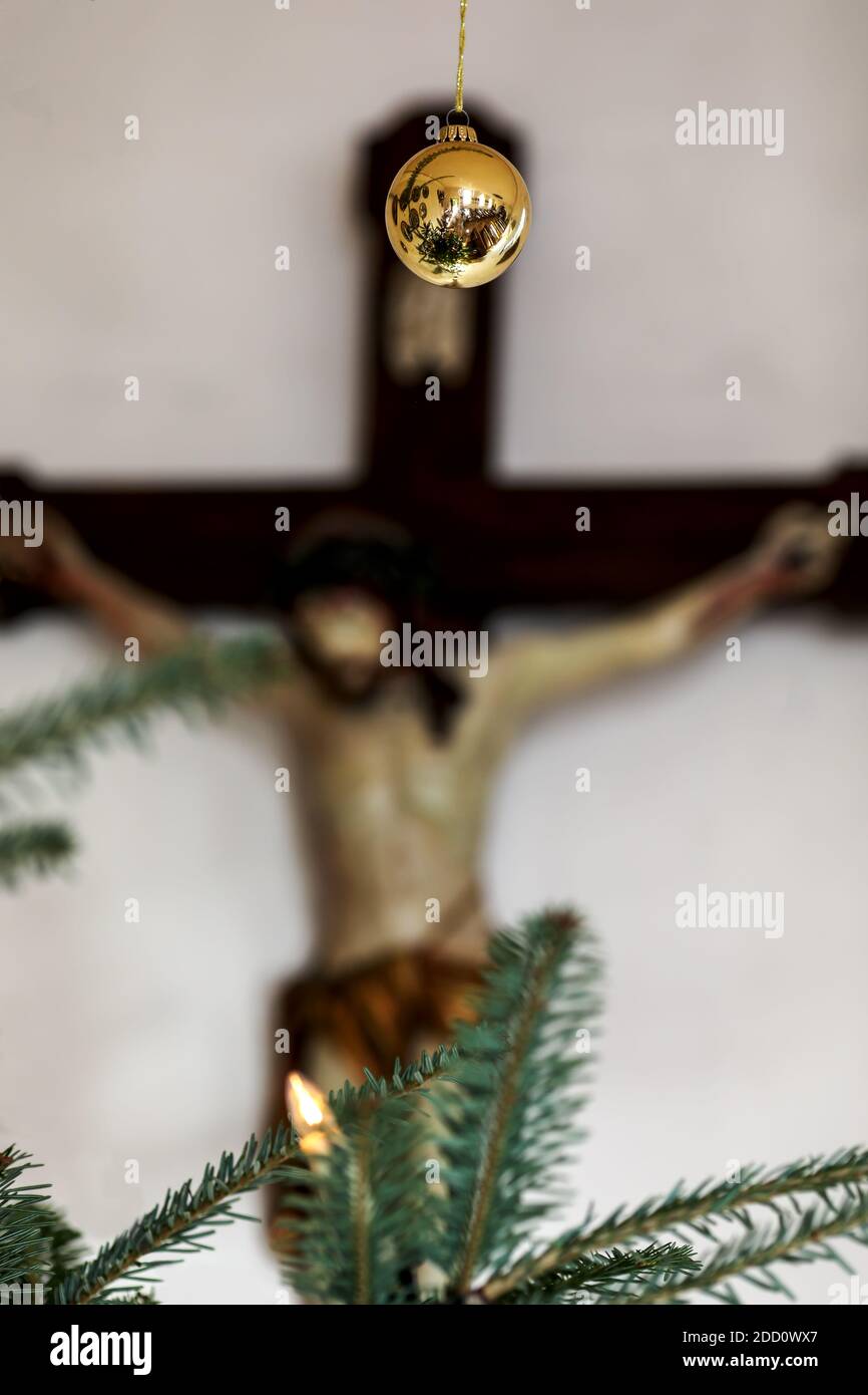 Singolo bauble dorato, sullo sfondo sfocato Gesù Cristo sulla croce, sul bordo inferiore dei rami dell'immagine dell'albero di natale Foto Stock