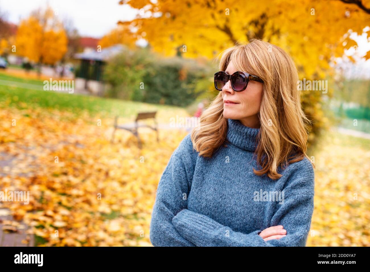 Ritratto di donna matura sicura con pullover e occhiali da sole a collo di turno mentre si trova nel parco in autunno. Foto Stock