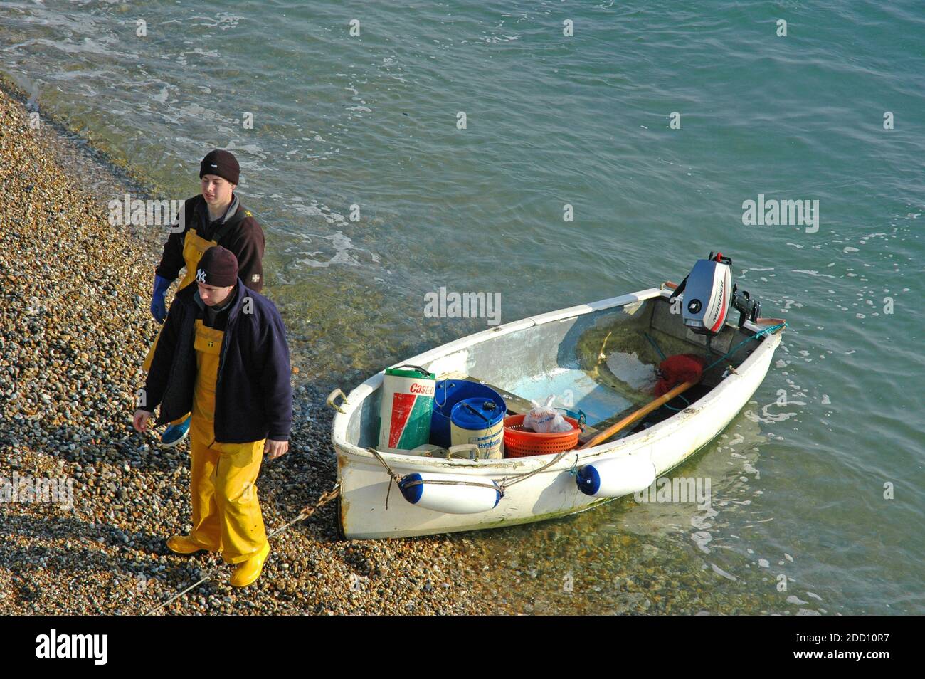 Due giovani pescatori Selsey, inglesi, che si sbarcarono dopo aver spiaggiato la piccola barca dopo la pesca del mattino. Selsey, Sussex occidentale. Inghilterra, febbraio. Modello Foto Stock