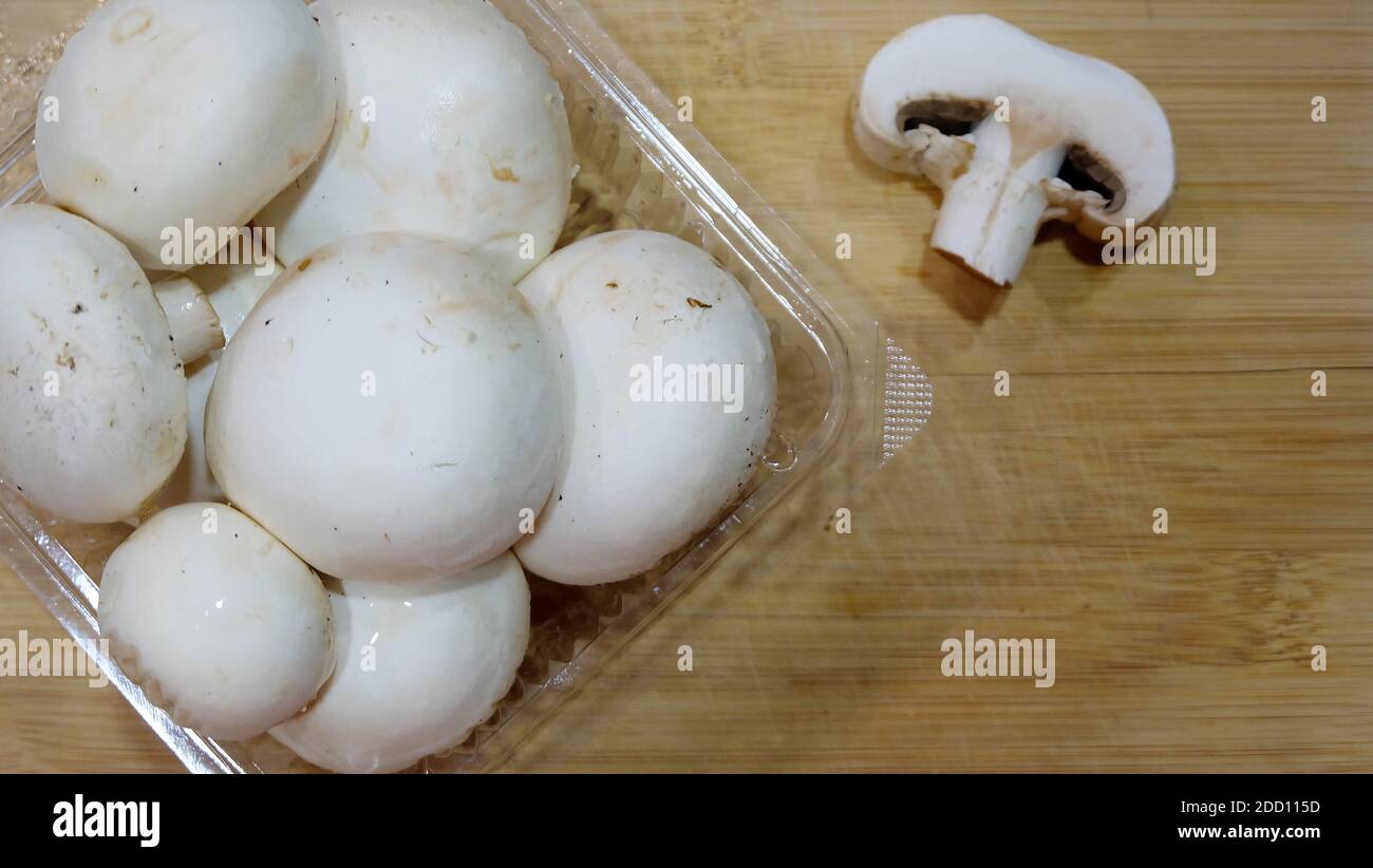 Primo piano di una confezione trasparente di funghi porcini bianchi, con coperchio aperto, posta sopra un tagliere di legno. Foto Stock