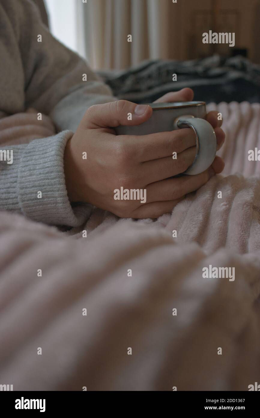 Primo piano di una tazza di caffè caldo pronto a bere. Ragazza avvolta con una morbida coperta in un giorno d'inverno sul suo divano. Accogliente casa al coperto 2020. Foto Stock