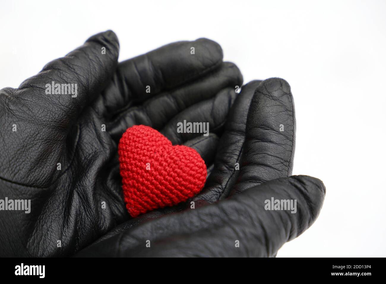 Cuore lavorato a maglia rosso nelle mani femminili in guanti di pelle nera su fondo di neve. Concetto di amore romantico, San Valentino, assistenza sanitaria in inverno Foto Stock