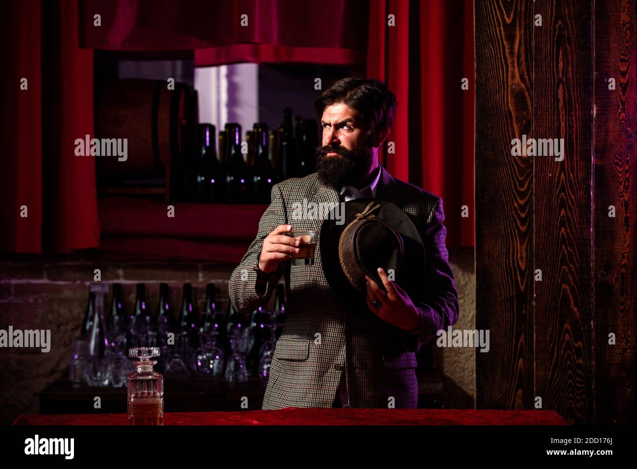 Uomo serio con un bicchiere di brandy. Uomo lavoratore vintage con barba lunga che tiene il whiskey. Seduto al bar. Foto Stock