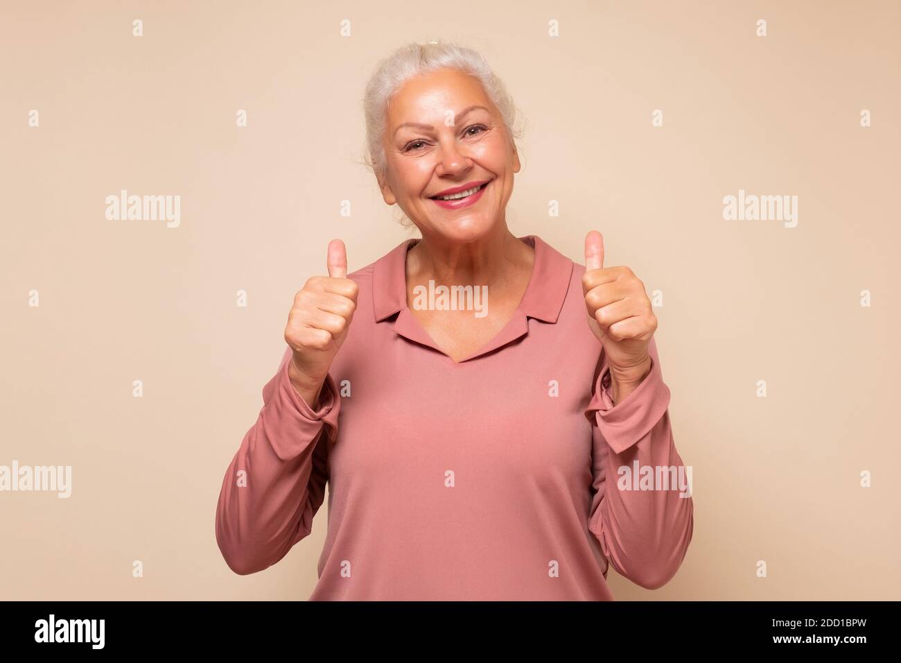 Donna anziana attiva che tiene il pollice in su approvando la vostra scelta. Emozione umana facciale positiva Foto Stock