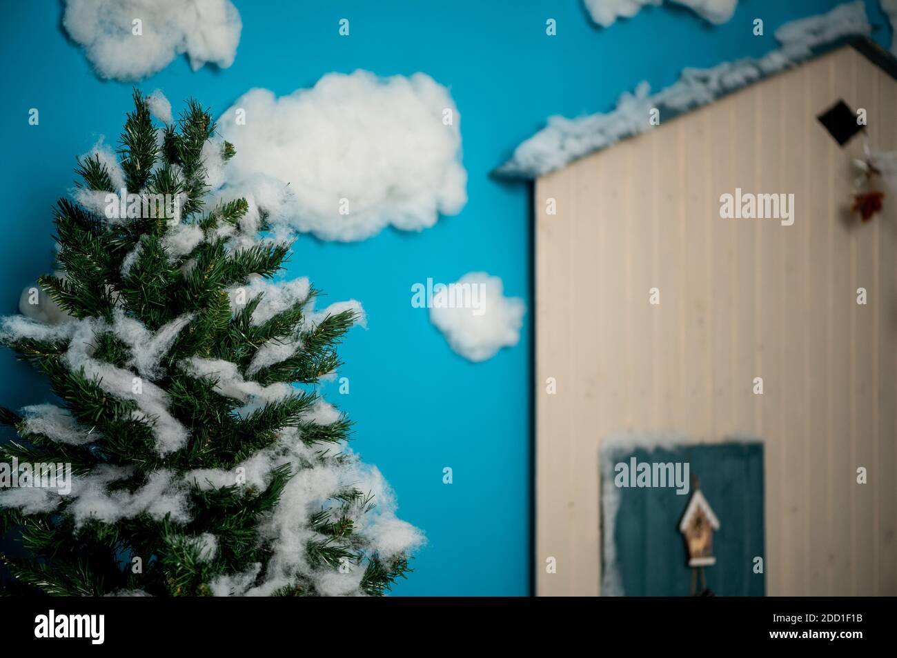 Studio decorativo di Natale con una casa con porta blu, panca in legno e sci, pupazzo di neve, nubi finte e neve Foto Stock