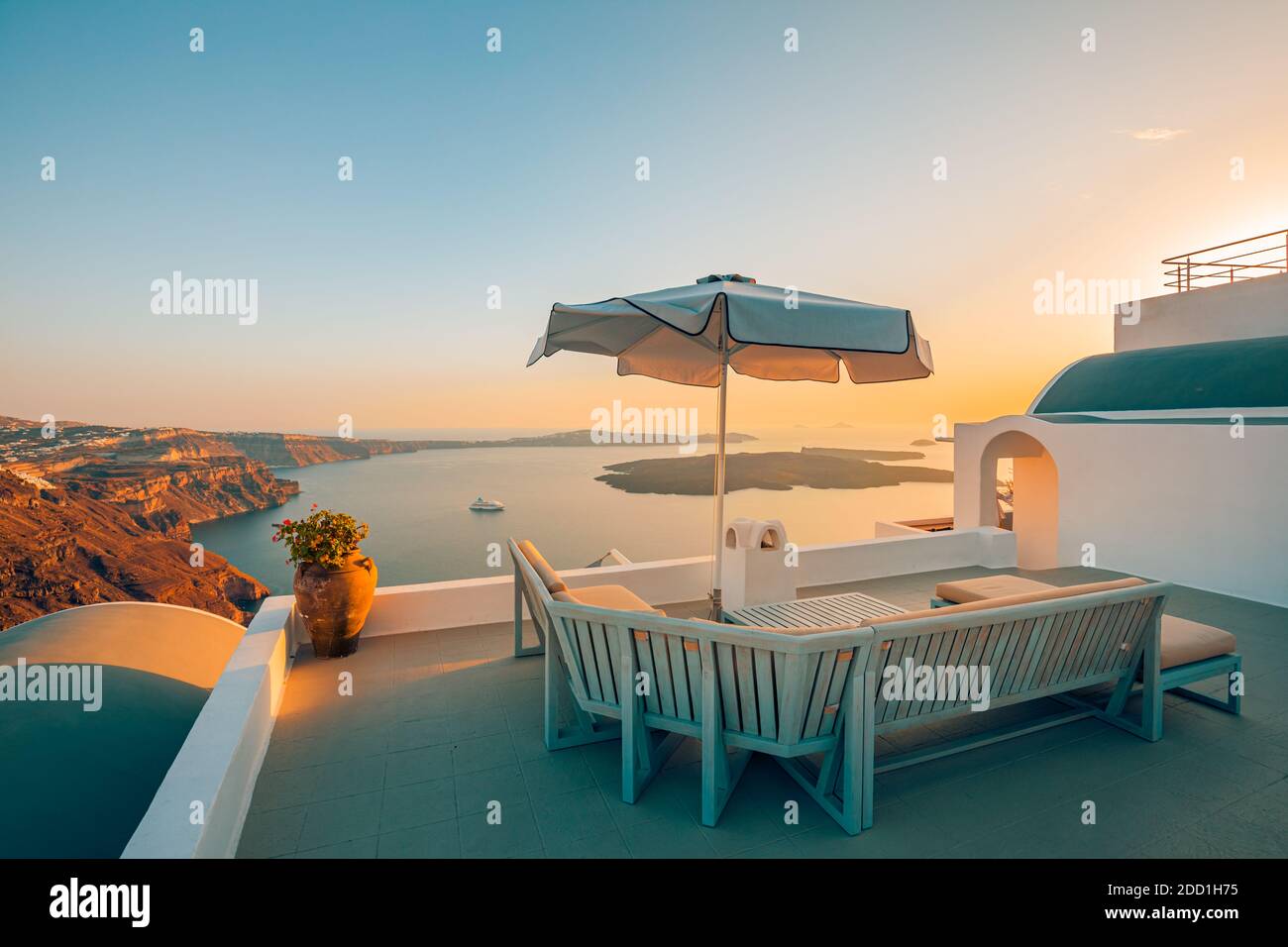 Terrazza al tramonto sull'isola di Santorini, Grecia. Splendido resort con vista sulla caldera e tramonto. Relax vibrazioni, ombrellone e sedie, tavolo. Vacanze estive Foto Stock