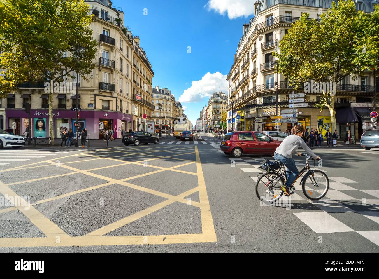 Un ciclista scorre attraverso un'intersezione lungo la Rue du Rivoli con auto e negozi su una soleggiata giornata estiva in Parigi Francia Foto Stock