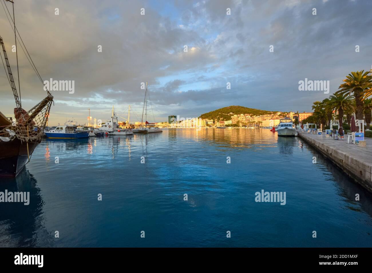 Il porto e passeggiata Riva mattina presto con le barche e l'acqua, le nuvole che si schiariscono e il sole del mattino che colpisce la città di Spalato Croazia Foto Stock