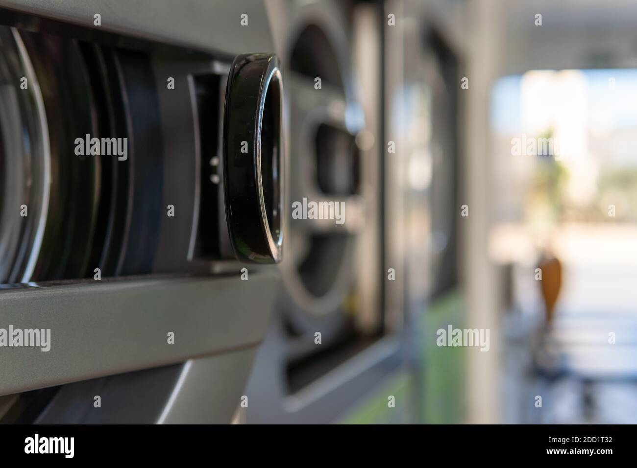 Particolare di una lavatrice industriale in primo piano, all'interno di una lavanderia con effetto bokeh Foto Stock