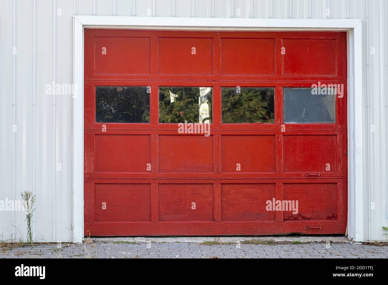 Una porta di garage in legno dipinta di rosso con finestre di vetro e maniglie in metallo è circondata da una parete bianca. Foto Stock