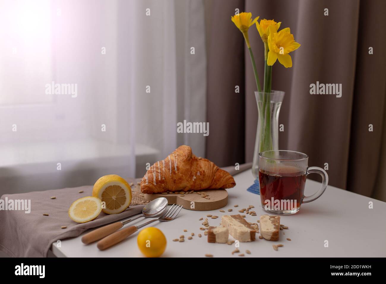 Prima colazione con una tazza di tè, croissant, limoni e narcis giallo in un vaso di vetro Foto Stock