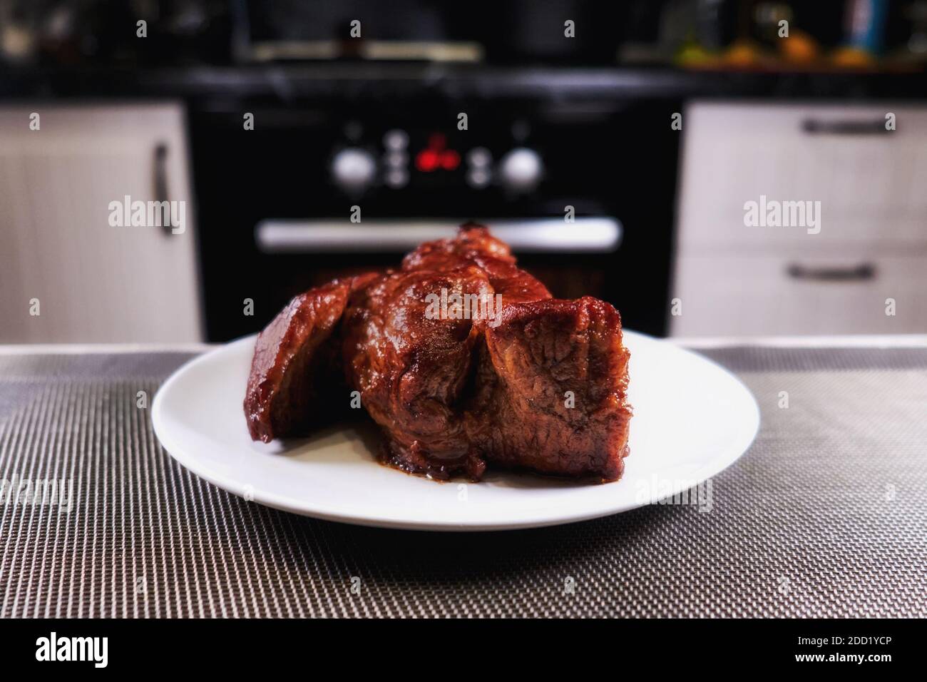 Bel pezzo di carne sul piatto. Primo piano di manzo arrosto. Barbecue di carne in cucina moderna. Forno a sfondo sfocato. Cena calda. Deliziosa bistecca su un wh Foto Stock