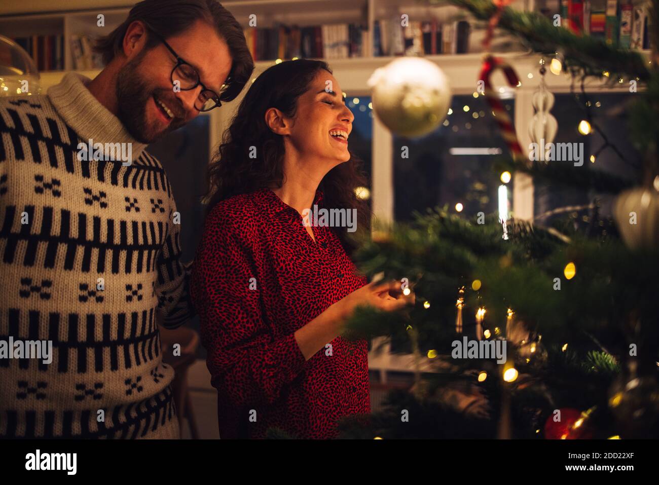 L'uomo e la donna sorridono mentre decorano l'albero di Natale a casa. Coppia godendo fare i preparativi della vigilia di Natale a casa. Foto Stock