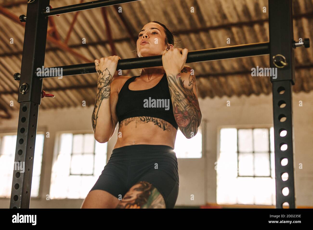 Femmina che fa tirare su l'allenamento in ombra di fabbrica vuota. Donna tatuata in abbigliamento sportivo che si esercita in un magazzino abbandonato. Foto Stock