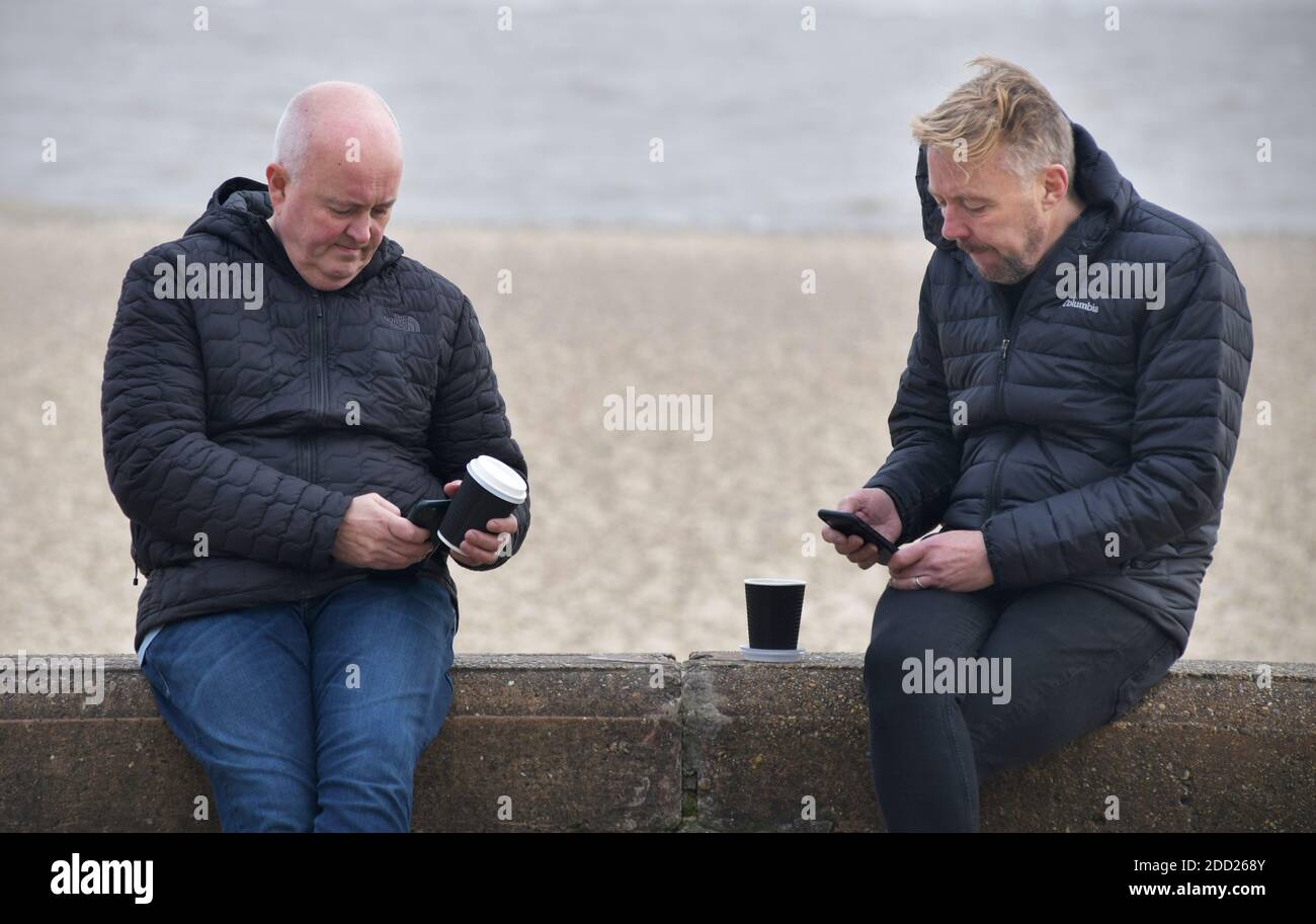 uomini di mezza età con tazze da caffè guardando il telefono cellulare schermi Foto Stock