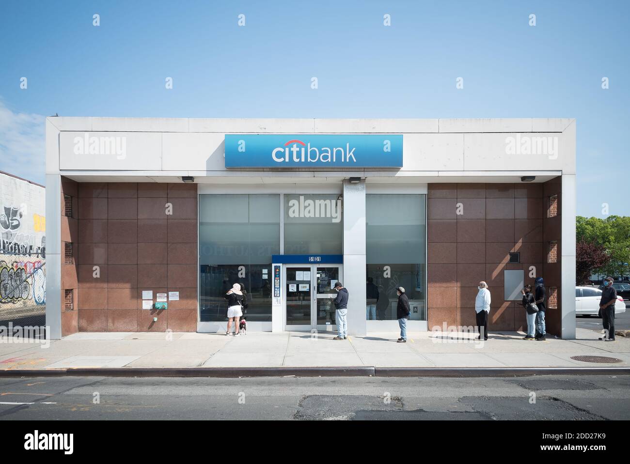 I clienti mantengono la distanza sociale e aspettano pazientemente in fila per entrare in una banca su Northern Boulevard, in Queens Foto Stock