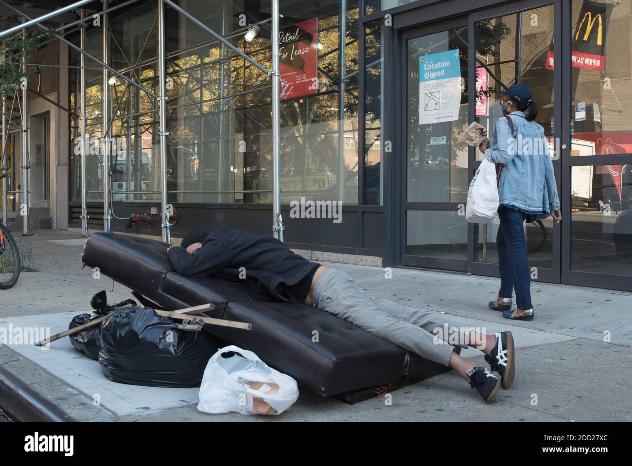 Manhattan, New York. 09 novembre 2020. Un uomo dorme su un divano disposto vicino a sacchi di spazzatura in Chelsea. Foto Stock