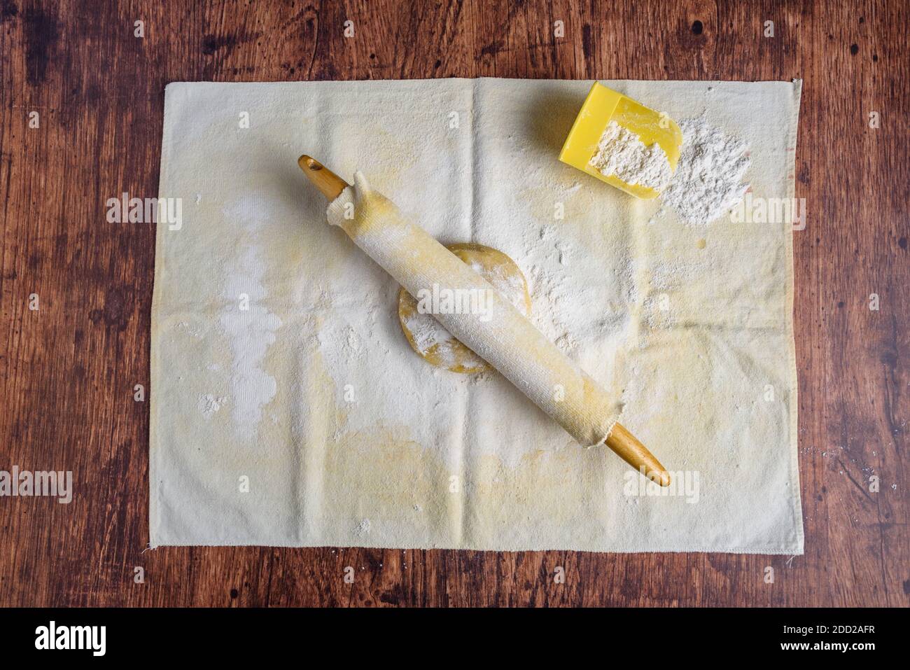 Preparazione per la cottura, palla di pasta di biscotti di zucchero su un panno di pasticceria e spilla di legno coperta su un tavolo di legno Foto Stock