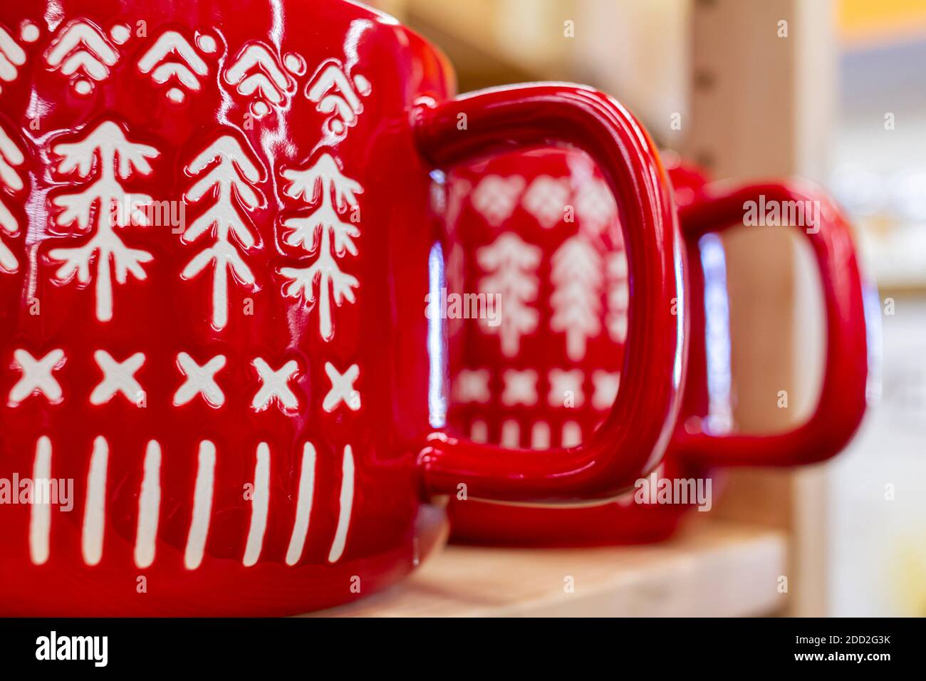 Due tazze da caffè in porcellana rossa lucida con manici affiancati su un ripiano. Hanno segni e texture bianche in forme di alberi di Natale di pino. Foto Stock