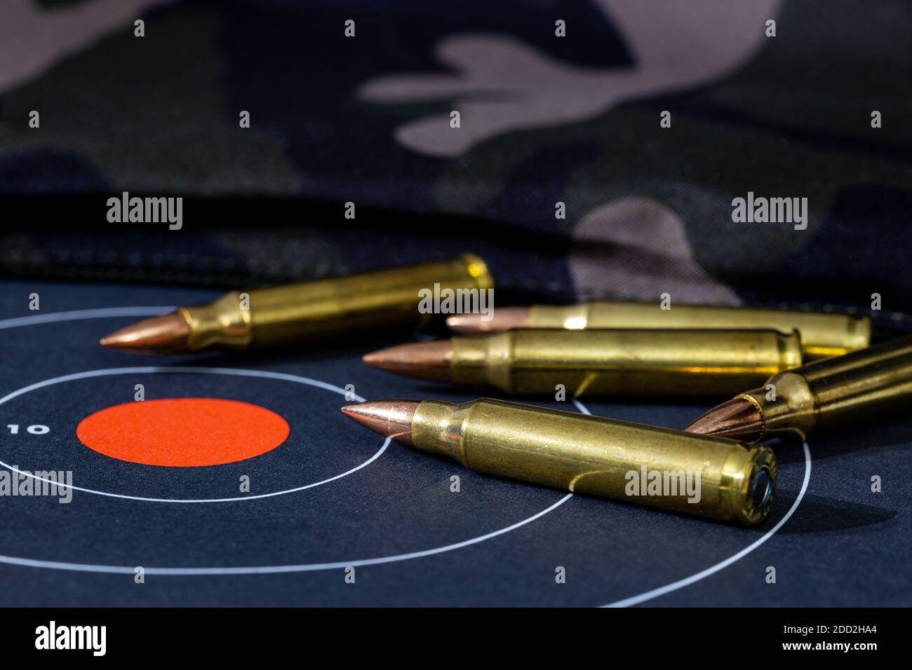 Giri sciolti di munizioni a fucile sparse sulla parte superiore di un bersaglio di carta con uno sfondo camouflage. Sfondo e primo piano sfocati con un punto di vista basso Foto Stock
