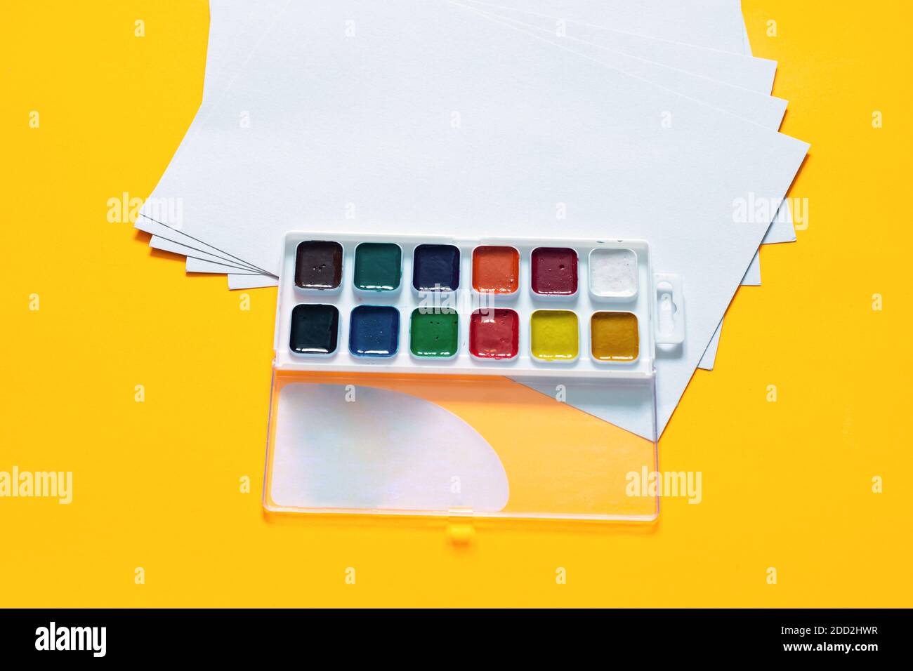 Fogli bianchi vuoti e 12 colori di vernice acquerello sopra uno sfondo giallo Foto Stock