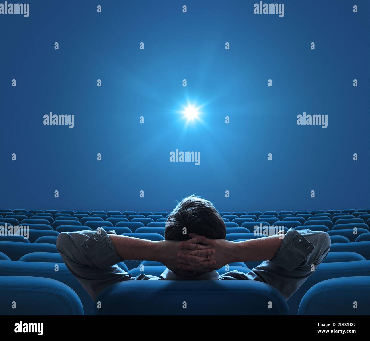 Cinema blu vuoto con una persona seduta al centro e che guarda sulla stella luminosa sullo schermo Foto Stock