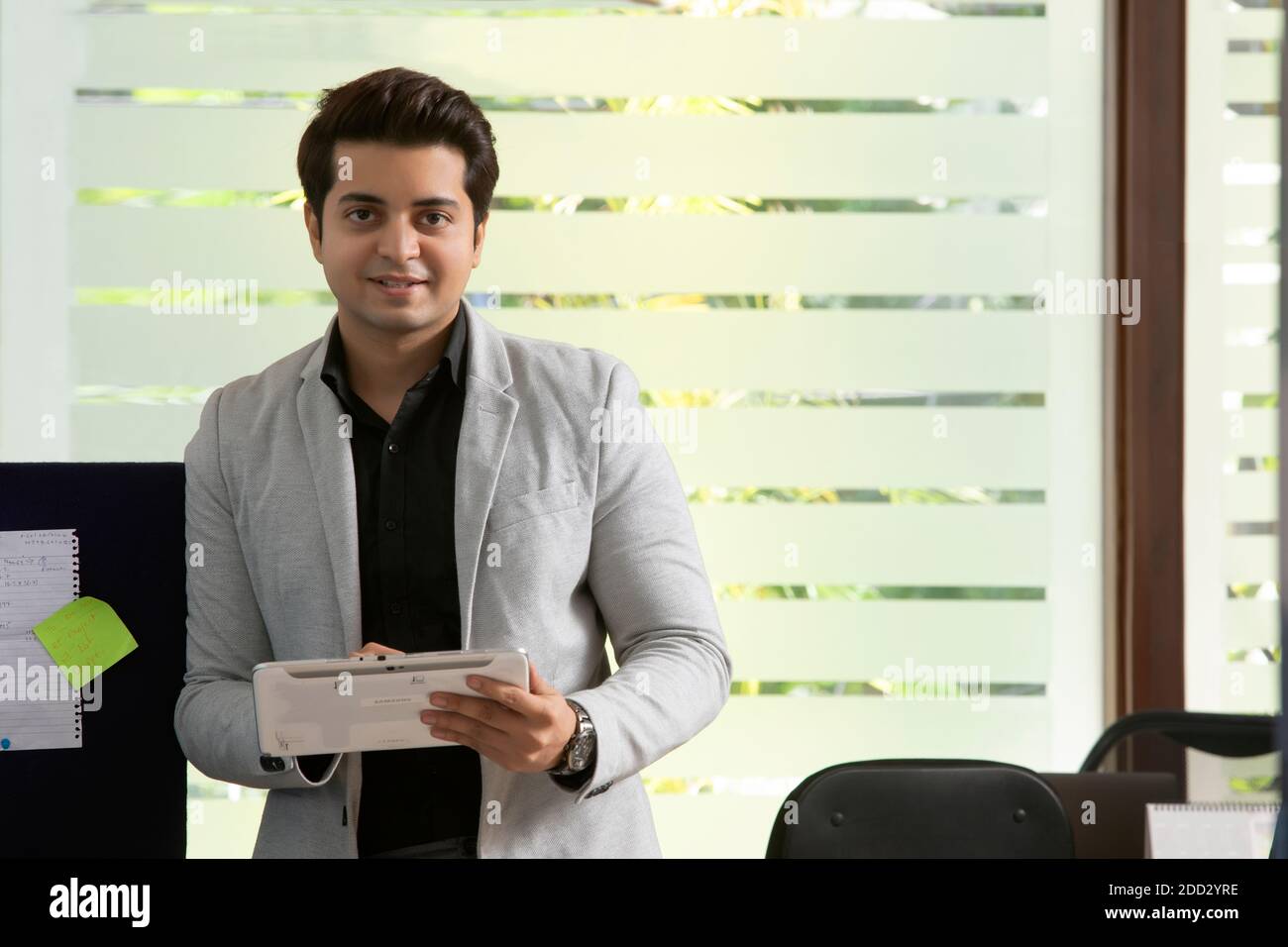 UN GIOVANE DIRIGENTE DELL'UFFICIO CHE TIENE UN TABLET DIGITALE GUARDANDO LA FOTOCAMERA E SORRIDENDO Foto Stock