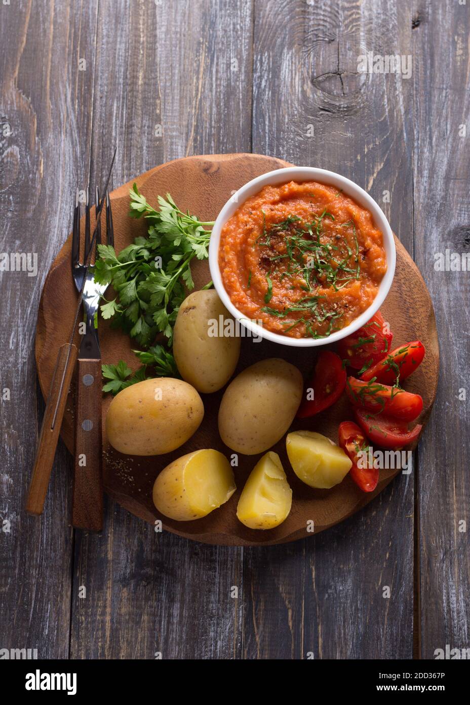 Patate giovani bollite in una buccia con caviale di zucchine o un tuffo di verdure, spezie, pomodori freschi e prezzemolo su una tavola di legno. Semplice e sano homema Foto Stock