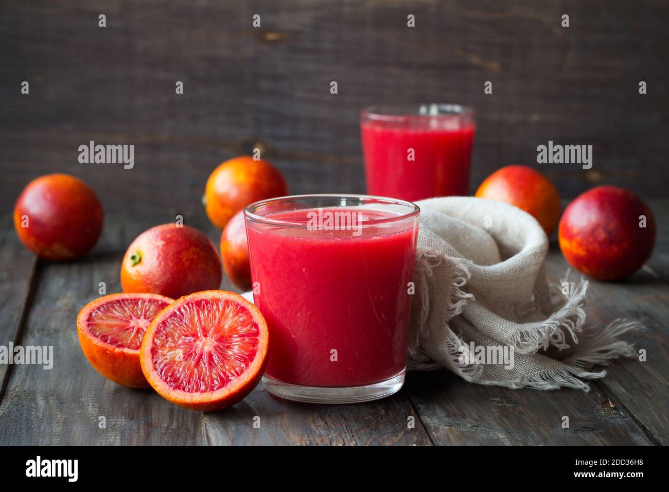 Spremuta fresca di arance di sangue in vetro con arance fresche intere su un tavolo di legno, fuoco selettivo Foto Stock